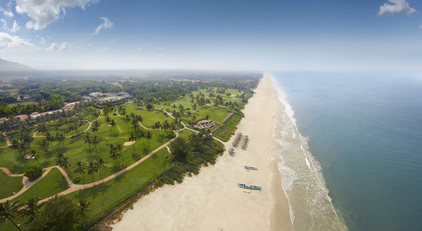 a high aerial shot looking down on a beach with golf course and resort behind it