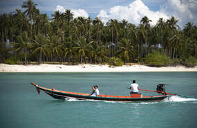 a longtail boat driving past a beach